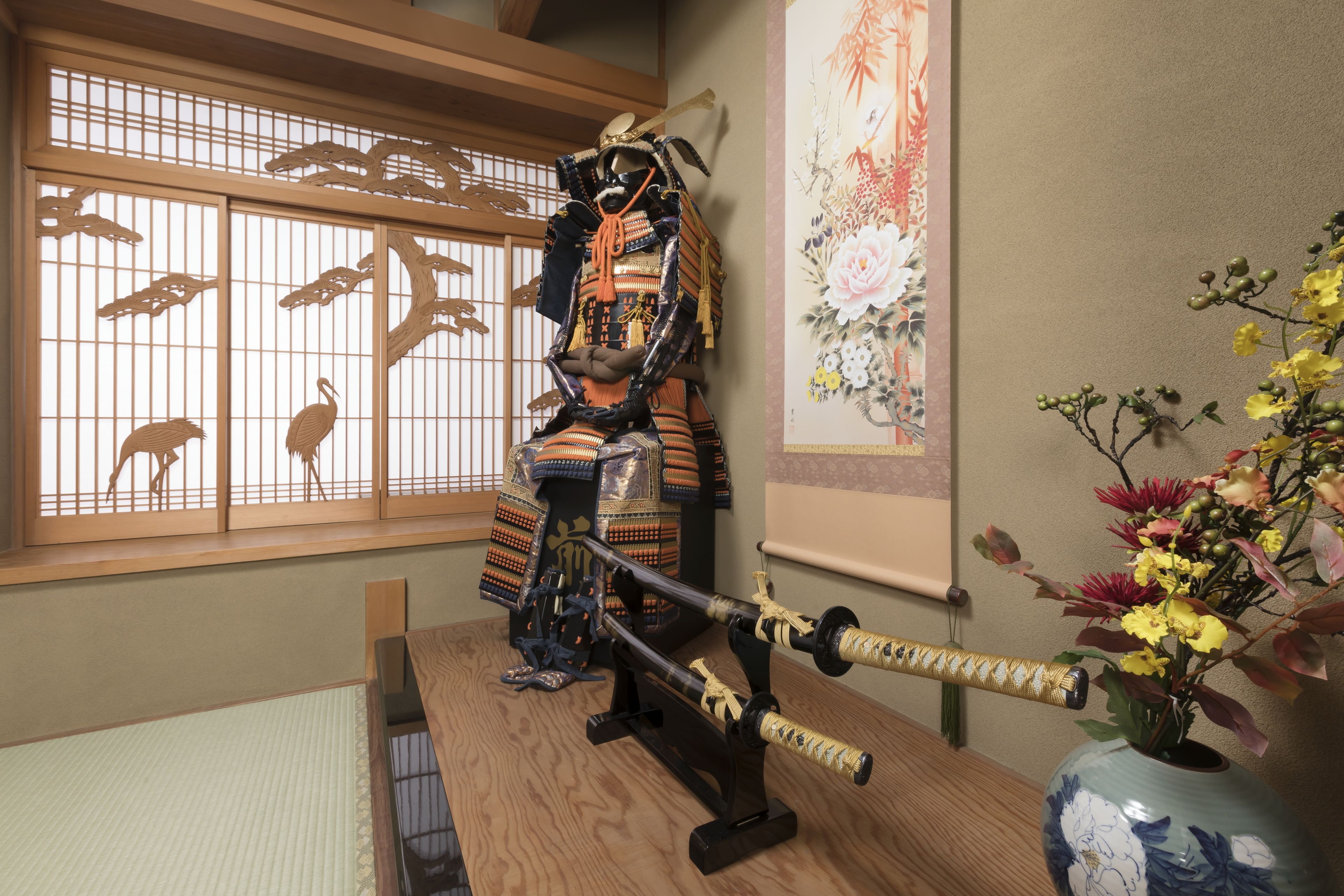 Een traditionele Japanse kamer met tatami vloerbedekking, een shoji scherm, een display met samurai harnassen en een vaas met bloemen.