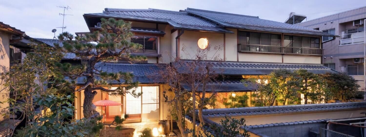 A traditional Japanese house with a tiled roof, a wooden balcony, and a small garden with a red umbrella.