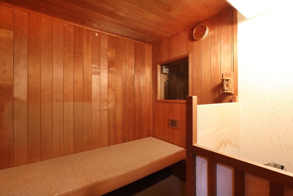 Una sauna de madera con un banco, un ventanal pequeño y un calentador en la pared.