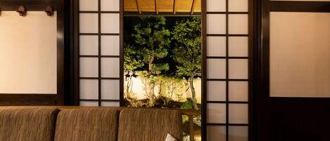 A traditional Japanese room with tatami flooring, a low wooden table, and a view through a shoji screen to a garden.