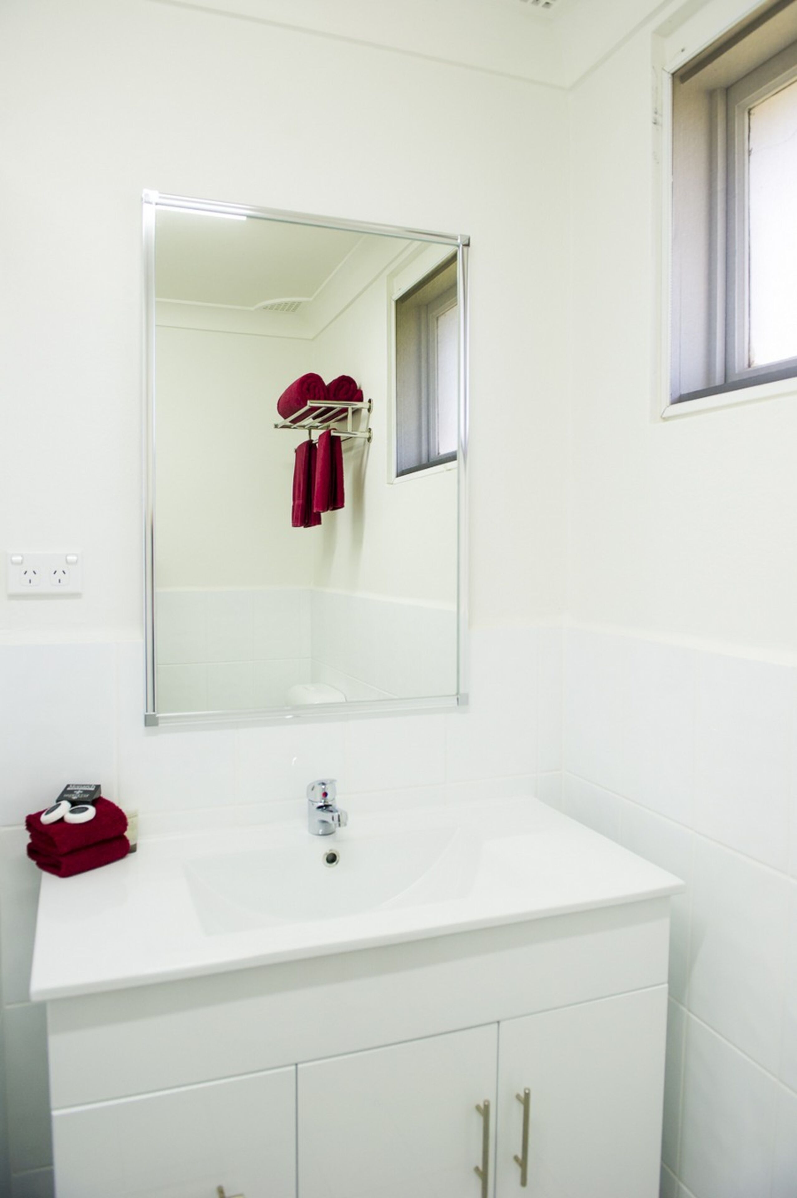 A bathroom with a white sink, a mirror, and a window.