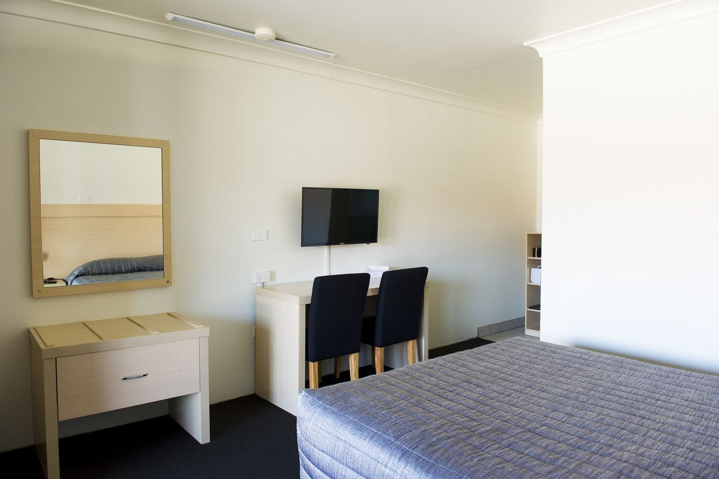 A hotel room with a bed, a desk with two chairs, a TV mounted on the wall, and a bedside table.