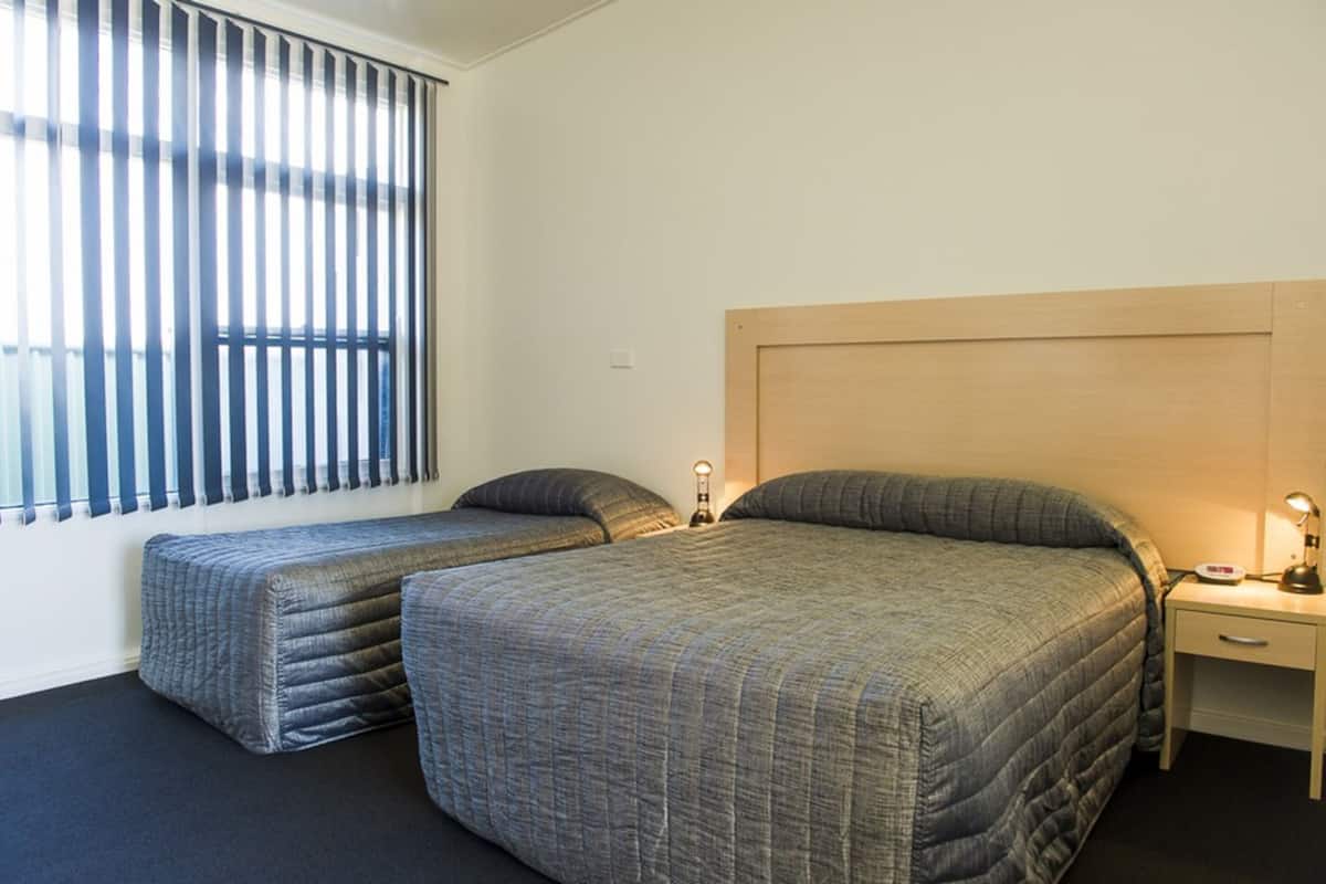 A room with two beds, a nightstand, a lamp, and a window with blinds.