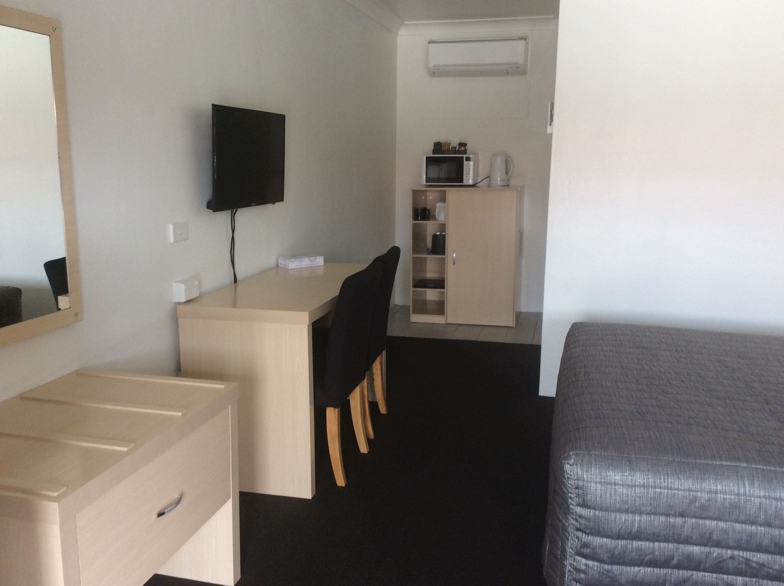 Ein kleines Hotelzimmer mit einem Bett, einem Schreibtisch mit Stuhl, einem Fernseher, einem Kleiderschrank und einer Mikrowelle.