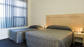 A room with two beds, a nightstand, and a window with blinds.
