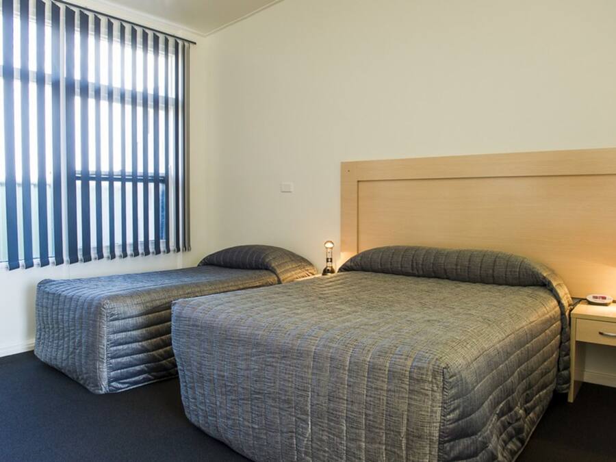 A room with two beds, a nightstand, and a window with blinds.