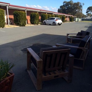A parking area with a row of wooden benches and a white car parked in the distance. - Cherry Blossom Motel (Young)