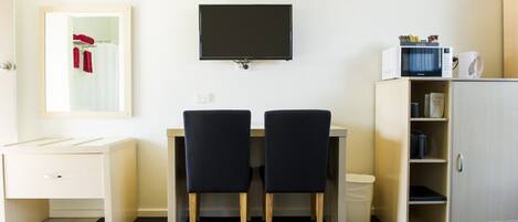 Une chambre d’hôtel comprenant un lit, un bureau avec deux chaises, une télévision, un four à micro-ondes et une armoire.