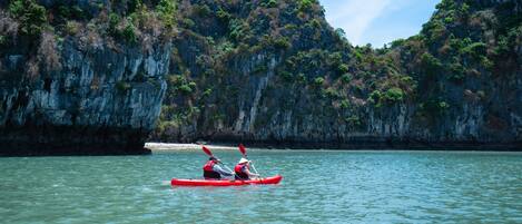 A kayaker in a red kayak on calm water with a rocky cliff in the background.
