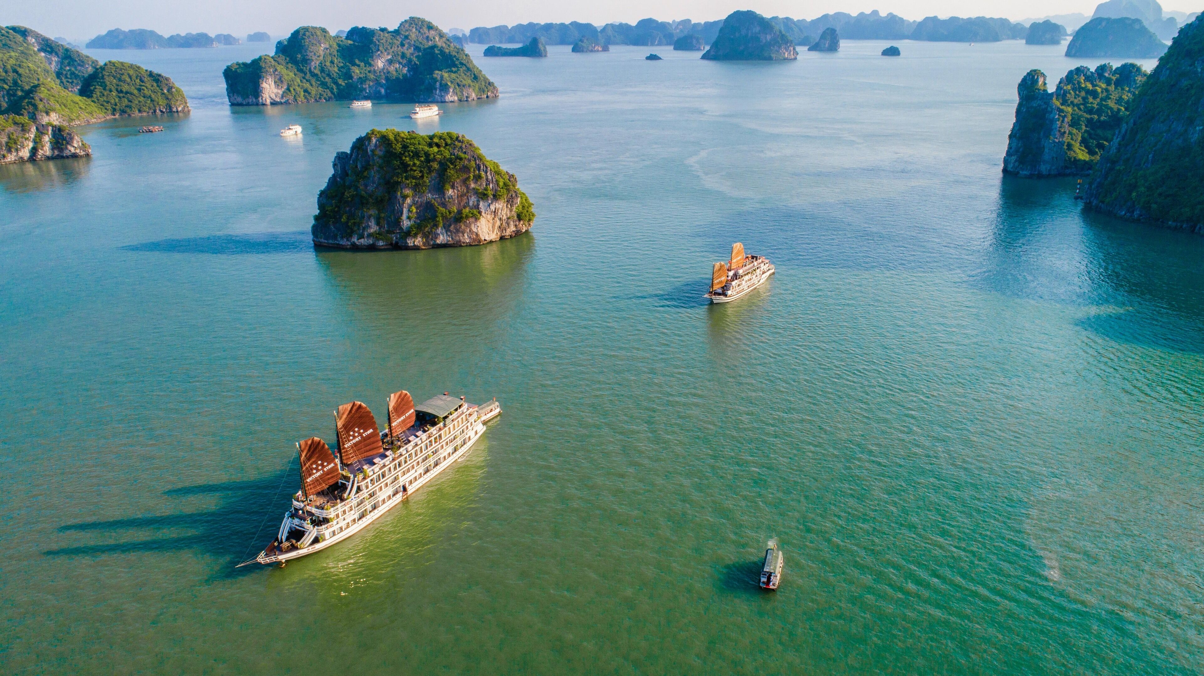 A river cruise ship with multiple decks and a large open deck area, surrounded by lush green islands and clear blue water.