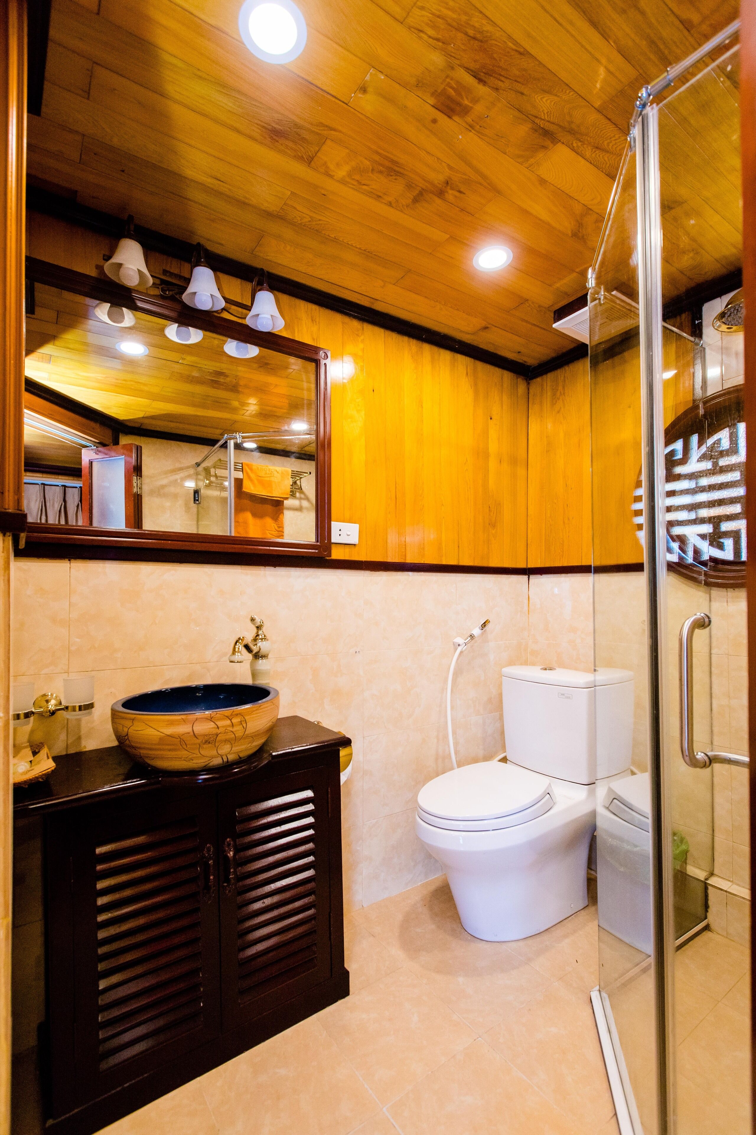 A bathroom with a wooden ceiling, a large mirror, a sink with a bowl, a toilet, and a shower area.