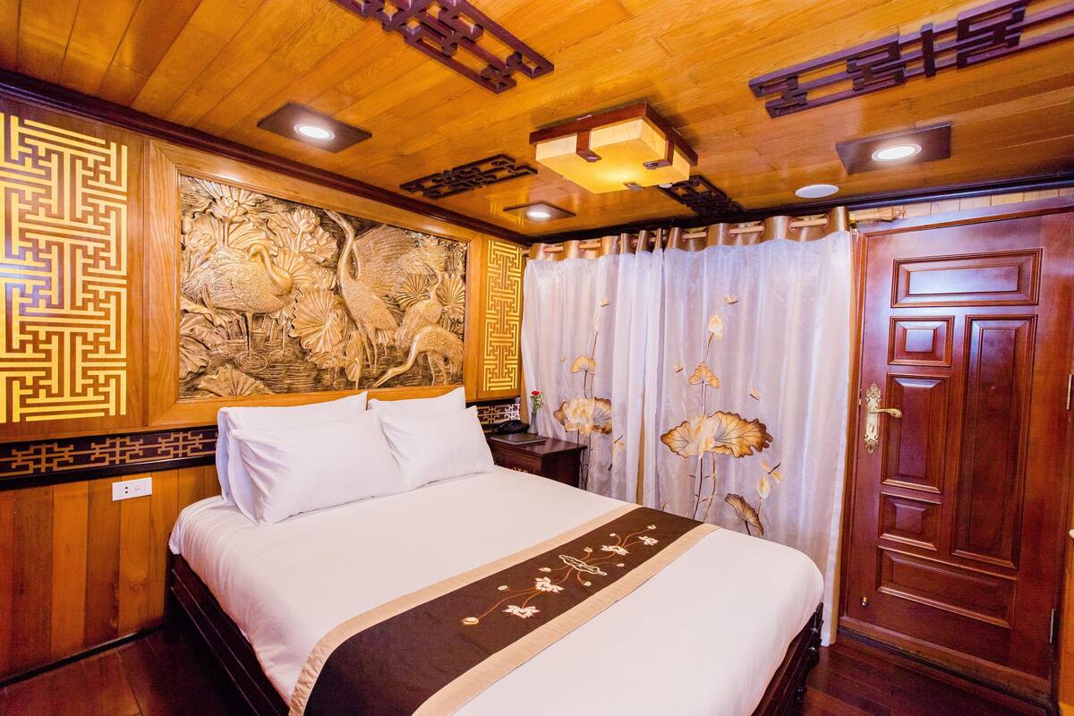 A hotel room with a wooden ceiling, a bed with white bedding, a decorative wall carving, and a wooden door.