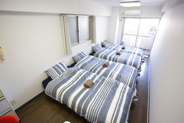 A hotel room with three beds, each with striped bedding and towels. There is a window with curtains, a wooden floor, and a white wall. - Castle Apartment Nezu (Tokyo)