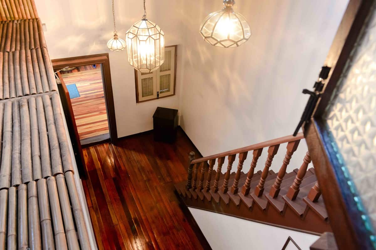 Un escalier en bois avec une rampe, un mur en bambou et deux luminaires suspendus.