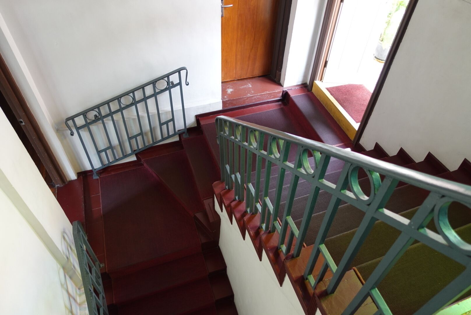 Un escalier avec des marches rouges et des rampes vertes, menant à une porte en bois.