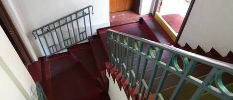 Un escalier avec des marches rouges et des rampes vertes, menant à une porte en bois.