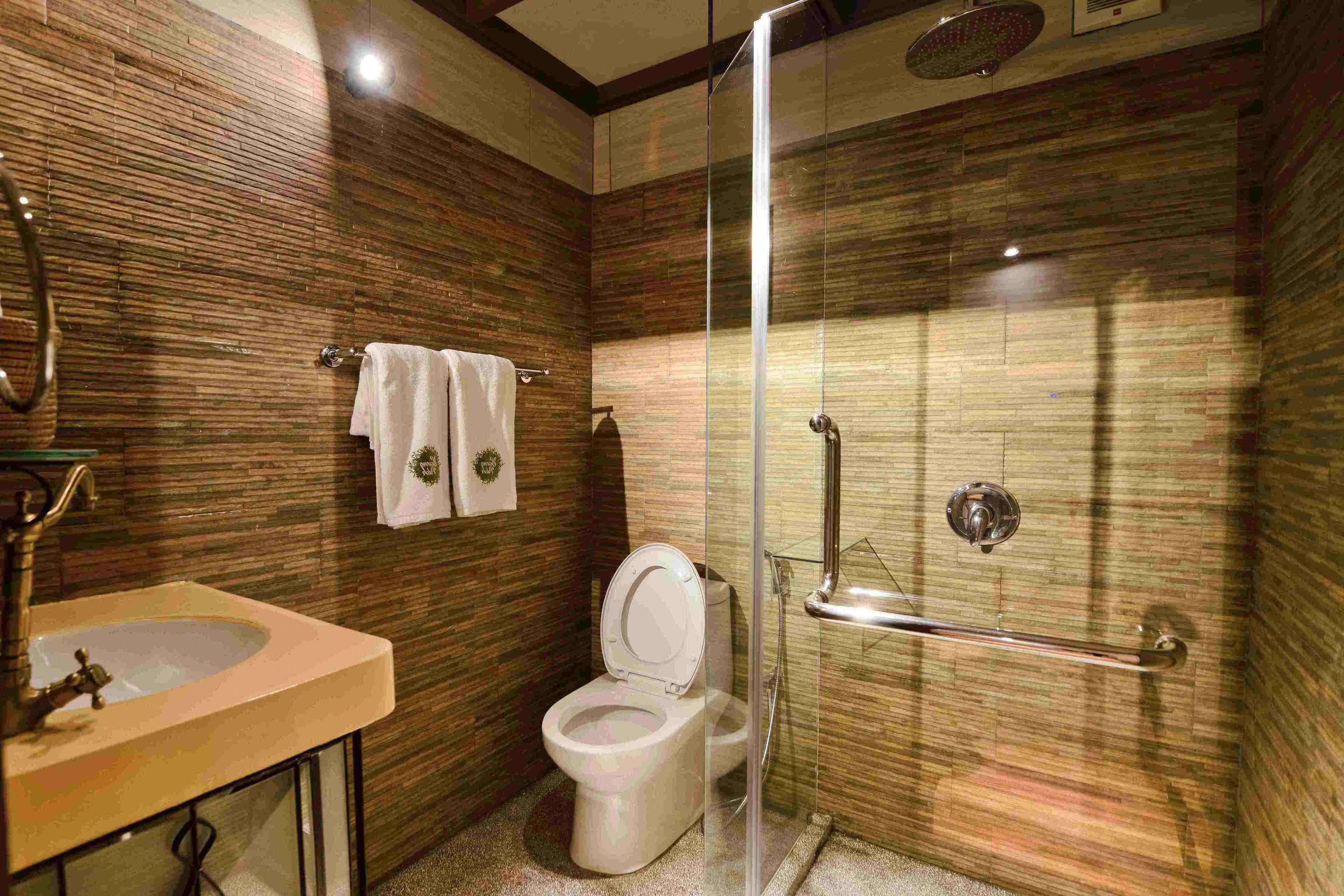 A bathroom with a wooden wall design, a toilet, a sink, and a glass-enclosed shower area.