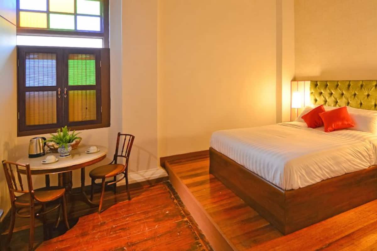 Une chambre d’hôtel comprenant un lit, une table de chevet, une lampe, une fenêtre avec stores et une petite table avec des chaises.