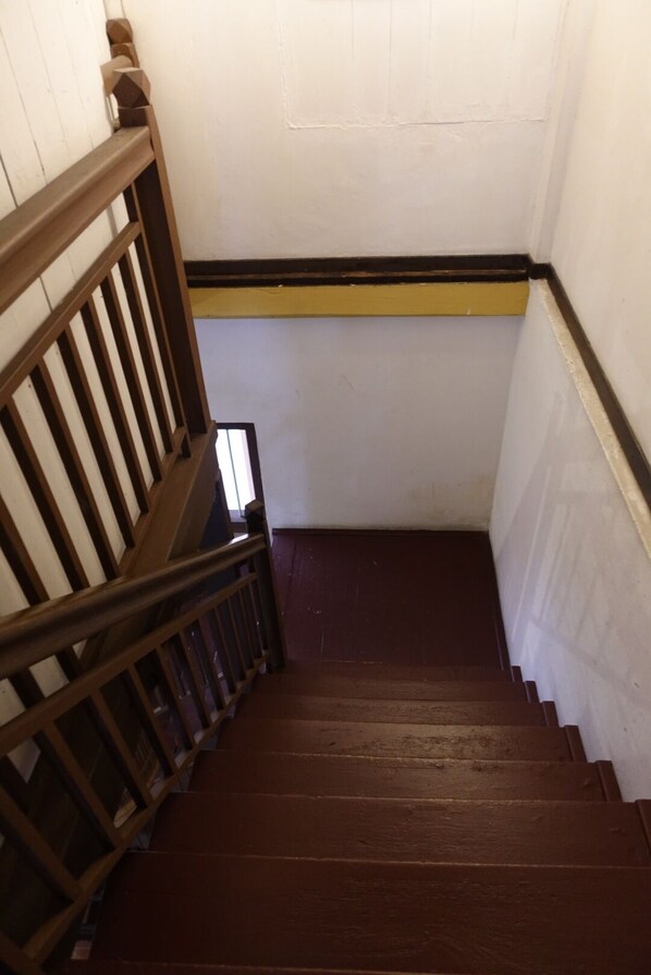 Una escalera de madera con barandilla, paredes blancas y una franja amarilla en la parte superior.