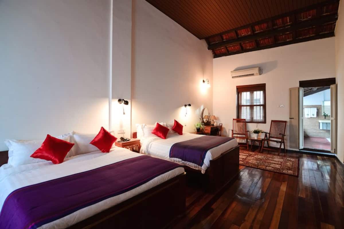Une chambre d’hôtel avec deux lits, un plancher en bois, une petite table avec des chaises et une vue sur l’extérieur.