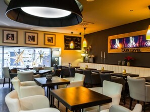 A modern cafe with tables and chairs, a large illuminated ceiling light, framed pictures on the wall, and a 'Cafe Level' sign.