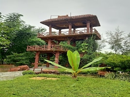 A wooden observation tower with a viewing platform, surrounded by lush greenery and a small pond.