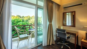 Habitación de hotel con balcón, escritorio, silla y vistas a zonas verdes.