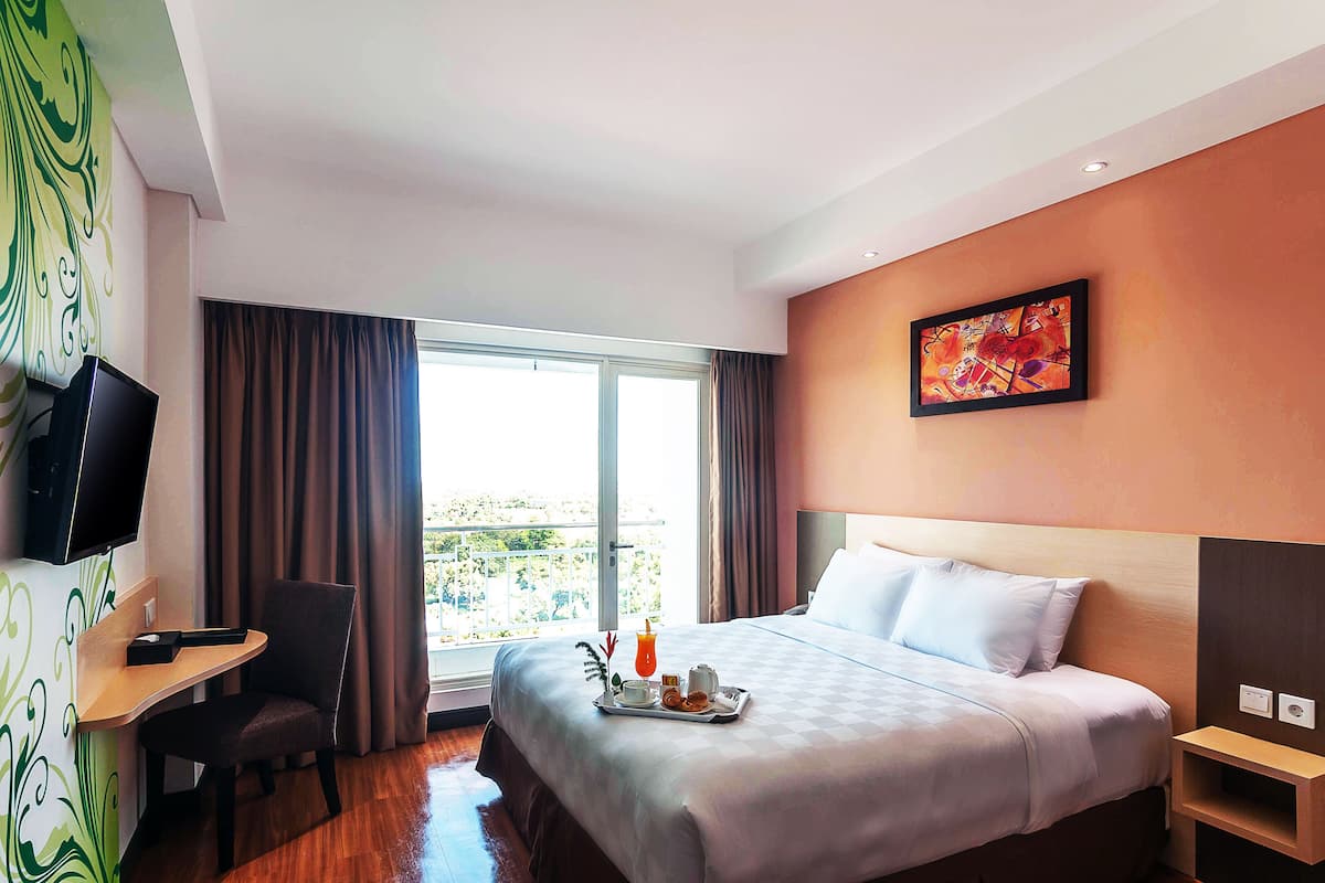 Una habitación de hotel con cama, escritorio, silla, televisor y ventana con cortinas.