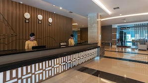 Zona de recepción de un hotel con diseño moderno, que incluye un mostrador de recepción, relojes y un cartel de recepción.