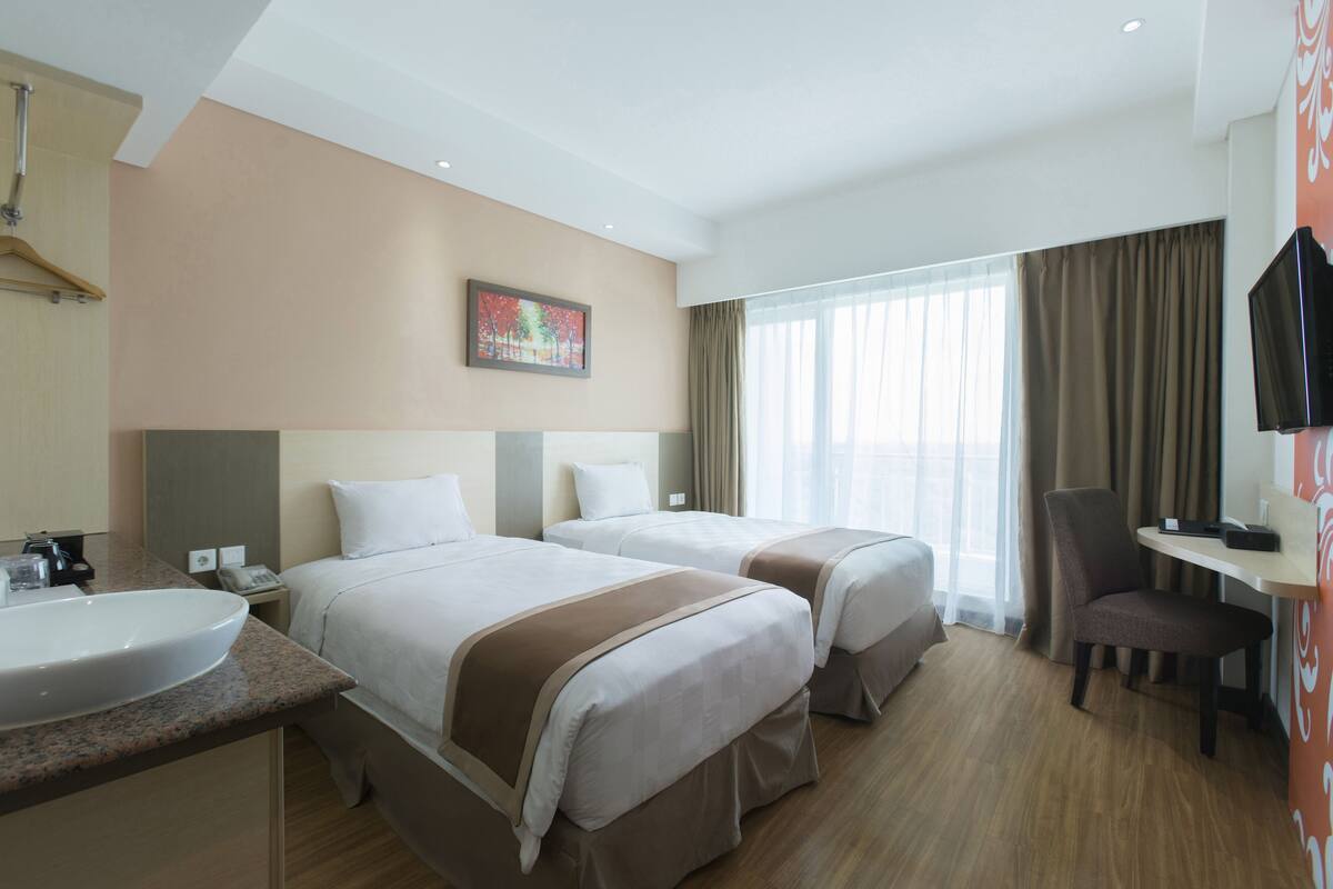 Habitación de hotel con dos camas, un escritorio, una silla, un televisor y un baño con lavamanos y espejo.
