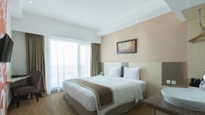 Habitación de hotel con una cama grande, un escritorio, una silla, un televisor, un cuadro y un baño con lavamanos.