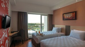 Habitación de hotel con dos camas, un escritorio con silla, televisión y balcón con vistas.