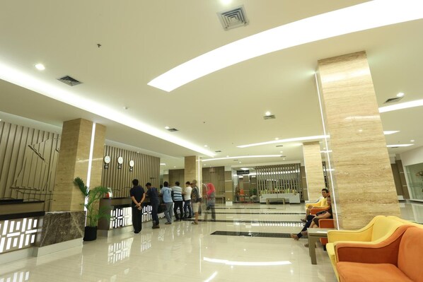 A modern lobby with a reception desk, seating area, and a large mirror. - Dalton Makassar (Makassar)