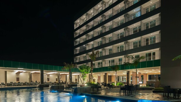 Un hotel de varios pisos con piscina, mobiliario exterior y un vestíbulo bien iluminado.
