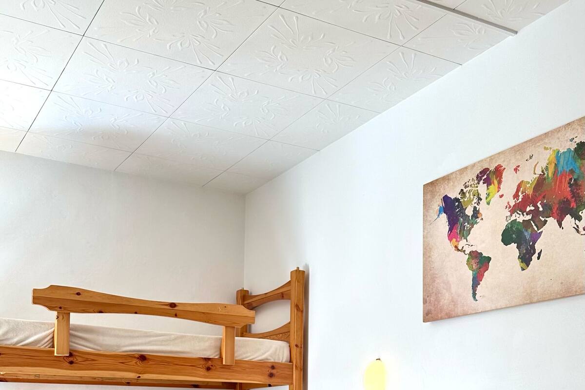 A room with a bunk bed, a single bed, a world map on the wall, and a ceiling with a floral pattern.