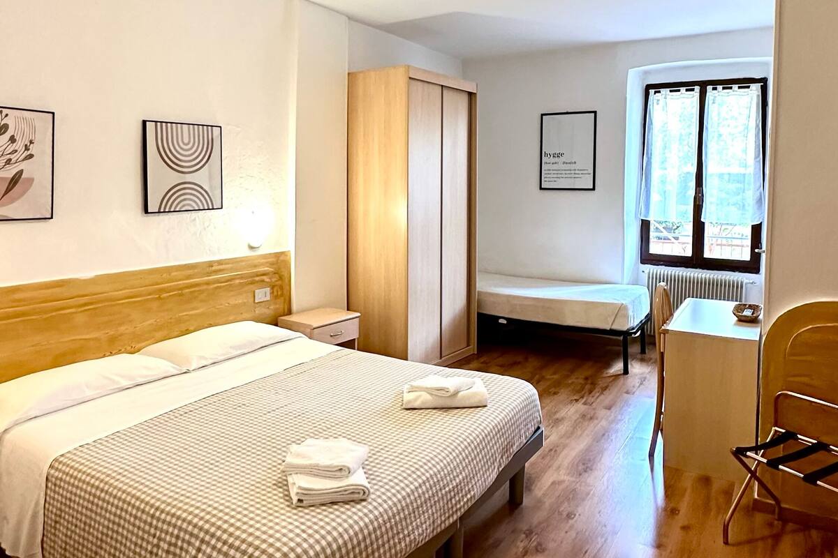 A hotel room with a bed, a desk, a chair, and a window with curtains.