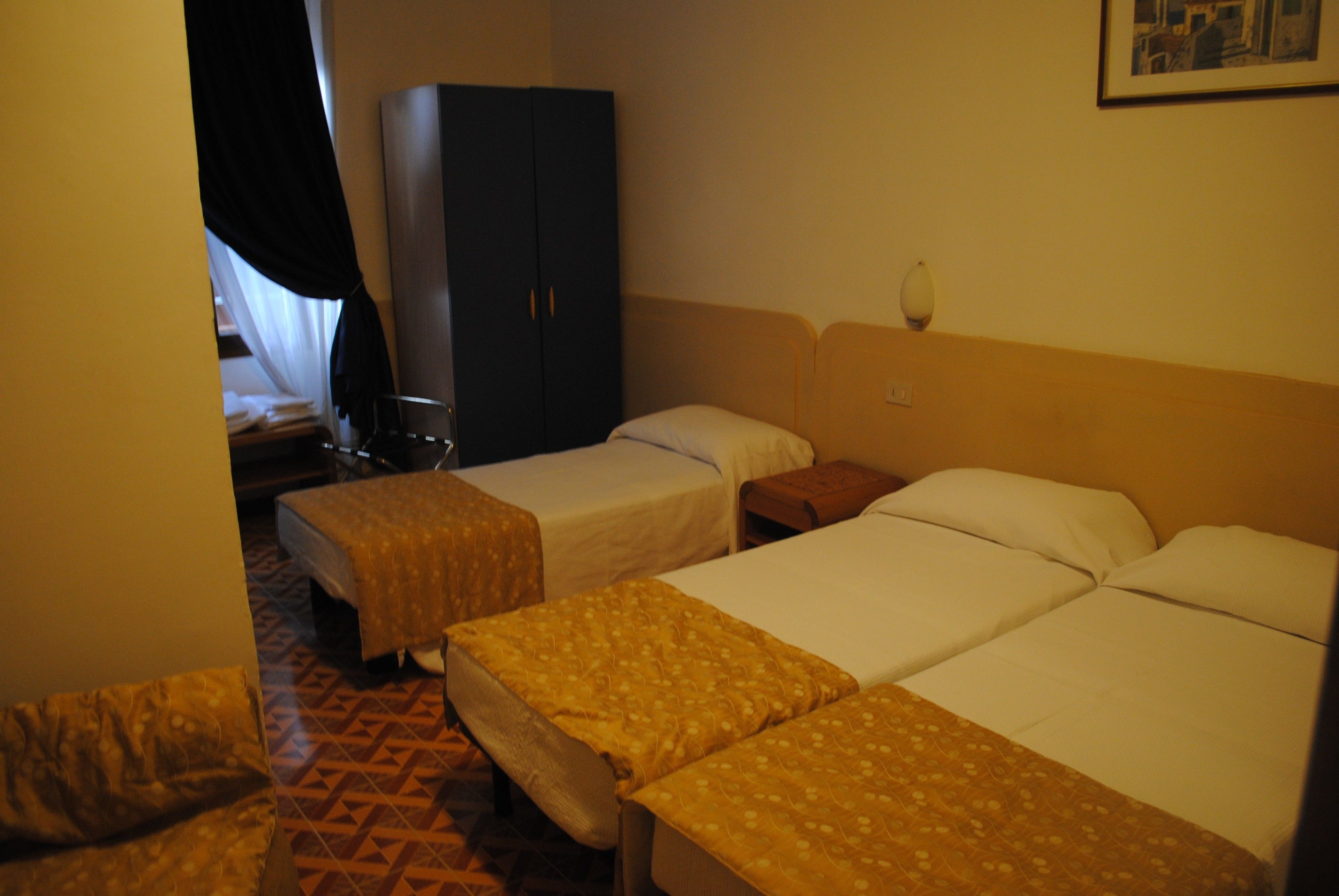 Una habitación de hotel con dos camas individuales, un armario, una mesita de noche y una silla.