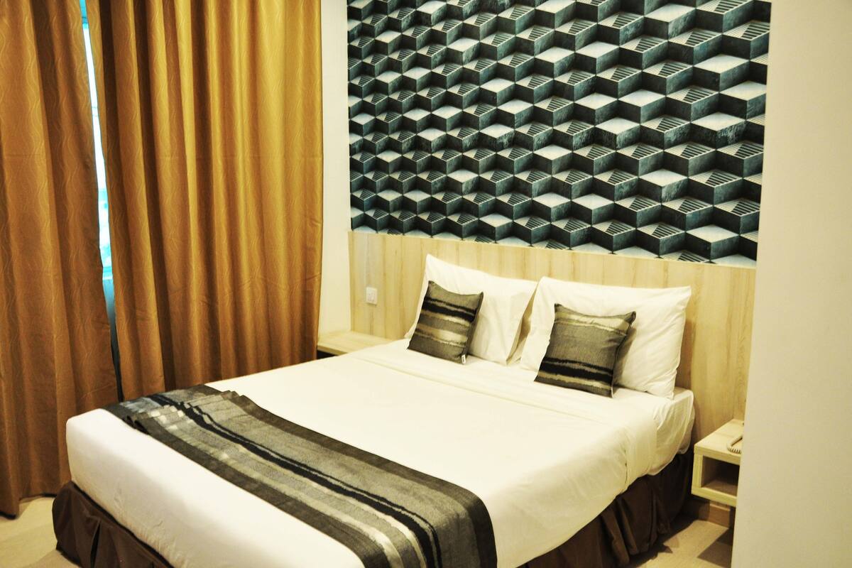 A hotel room with a bed, curtains, a nightstand, and a wall with a geometric pattern.