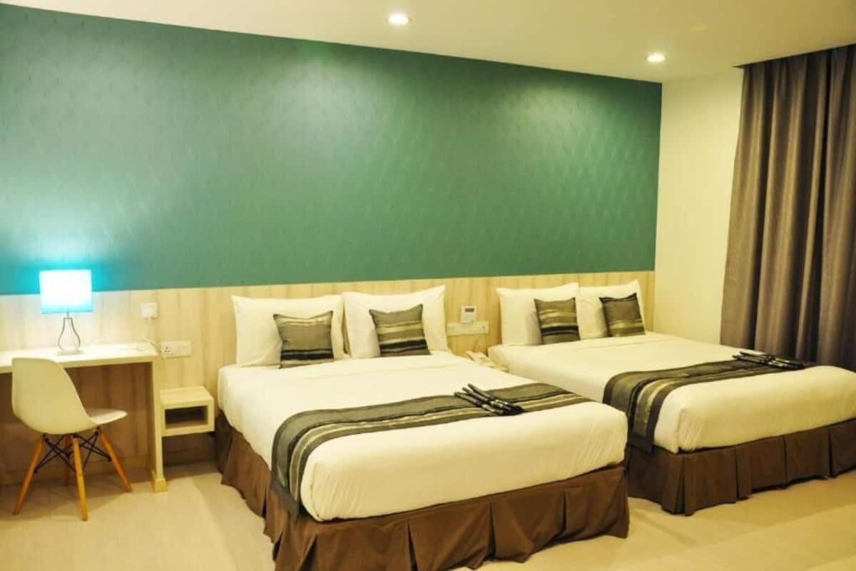 A hotel room with two beds, a desk, a chair, and a lamp.