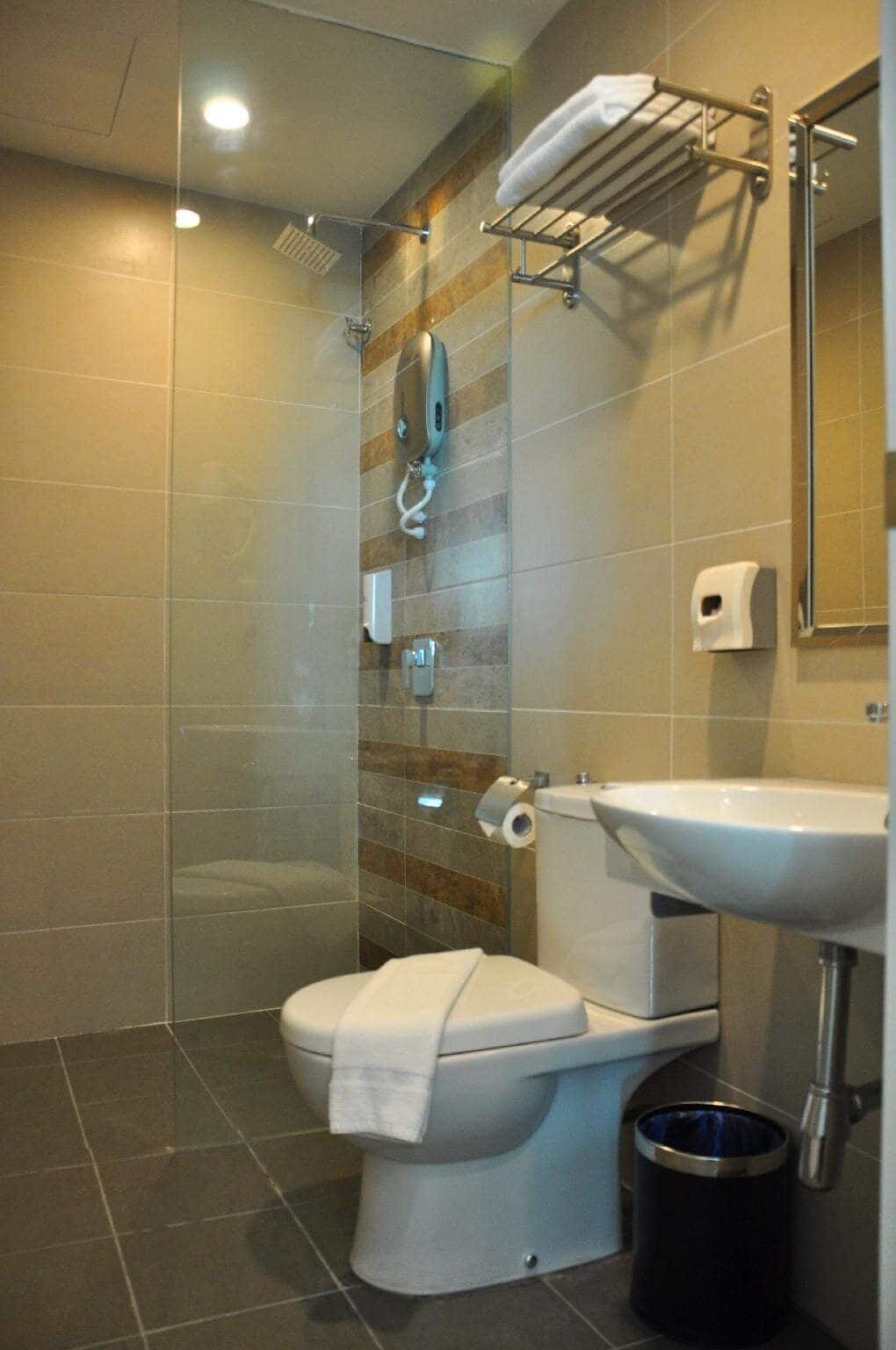 Un baño moderno con cabina de ducha de vidrio, un inodoro blanco, un lavamanos y un perchero para toallas.