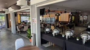 Un restaurante con mesas, una zona de bufé y una barra con equipo para servicio de alimentos.