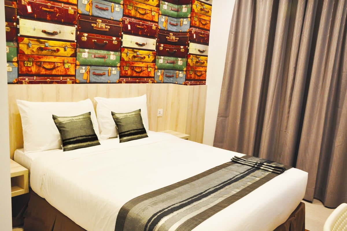 A hotel room with a large bed, two pillows, a bedside table, and a wall decorated with vintage suitcases.