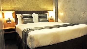 A neatly made bed with a striped pillow and a bedside table with a lamp.