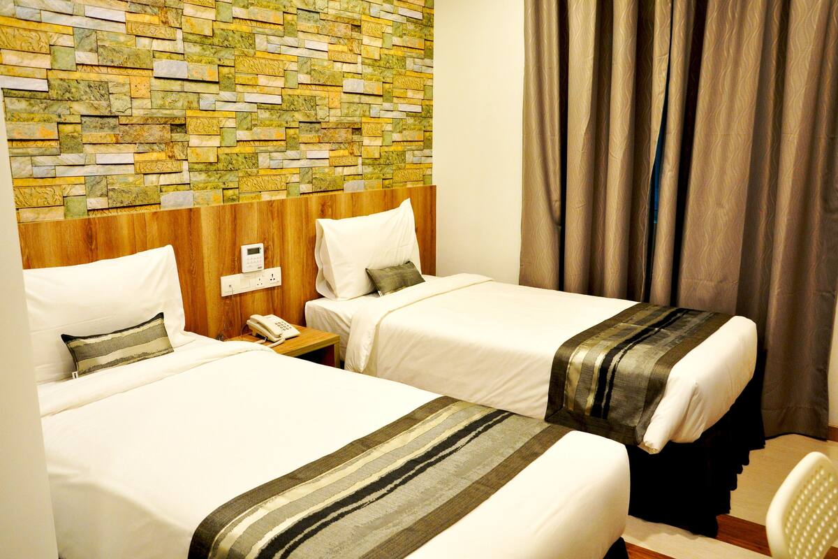 A hotel room with two beds, a stone wall, a wooden headboard, a telephone, and a curtain.