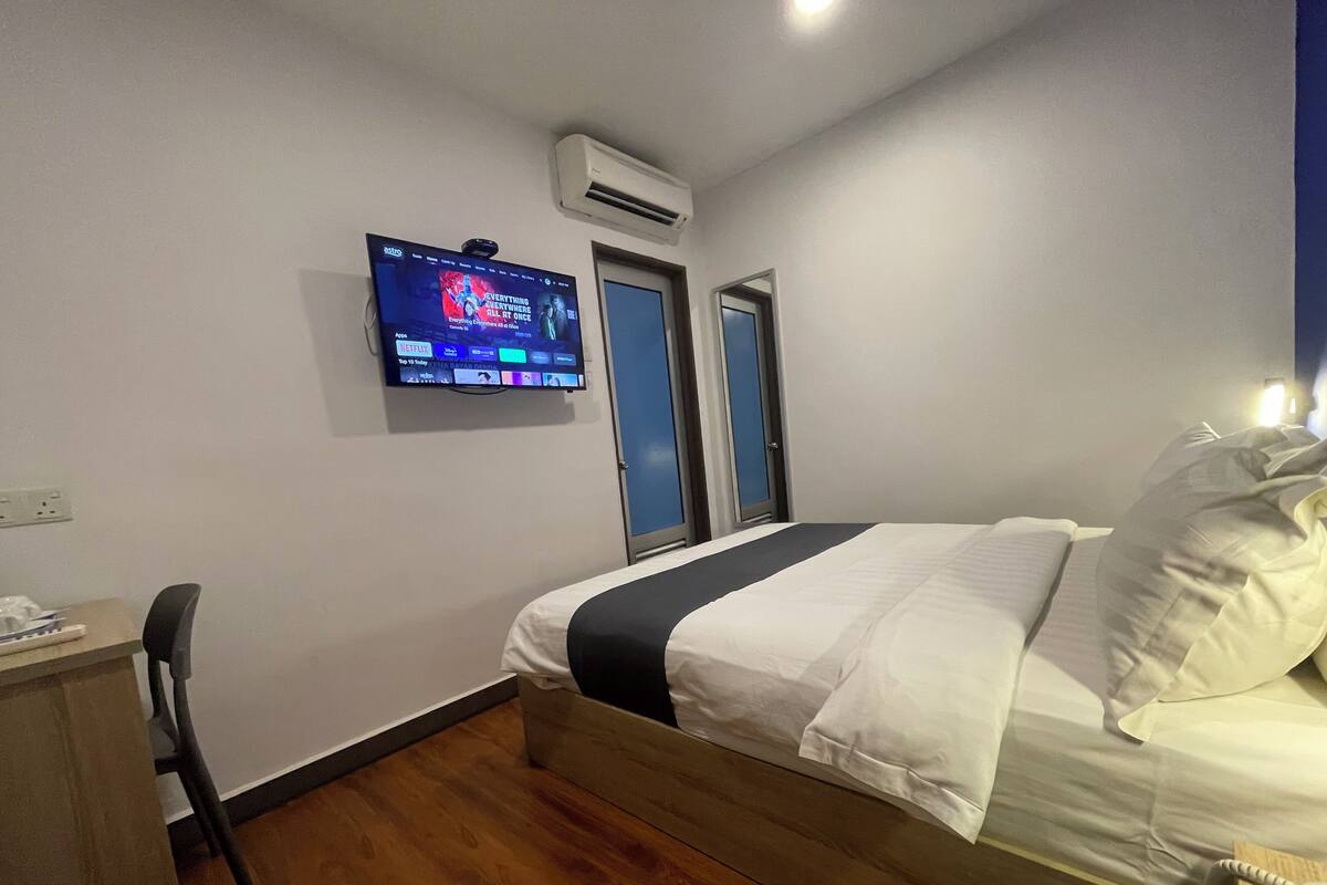 Une chambre d’hôtel équipée d’un lit, d’un bureau, d’une chaise, d’un téléviseur fixé au mur et d’un appareil de climatisation.