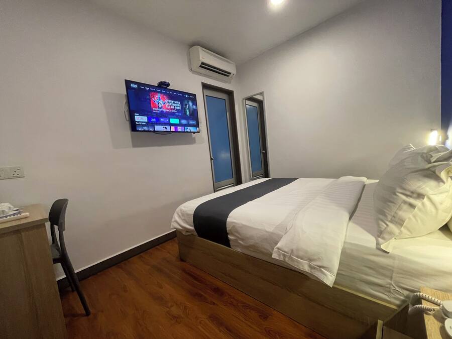 Quarto de hotel com cama, escrivaninha, cadeira, TV fixada na parede e ar-condicionado.