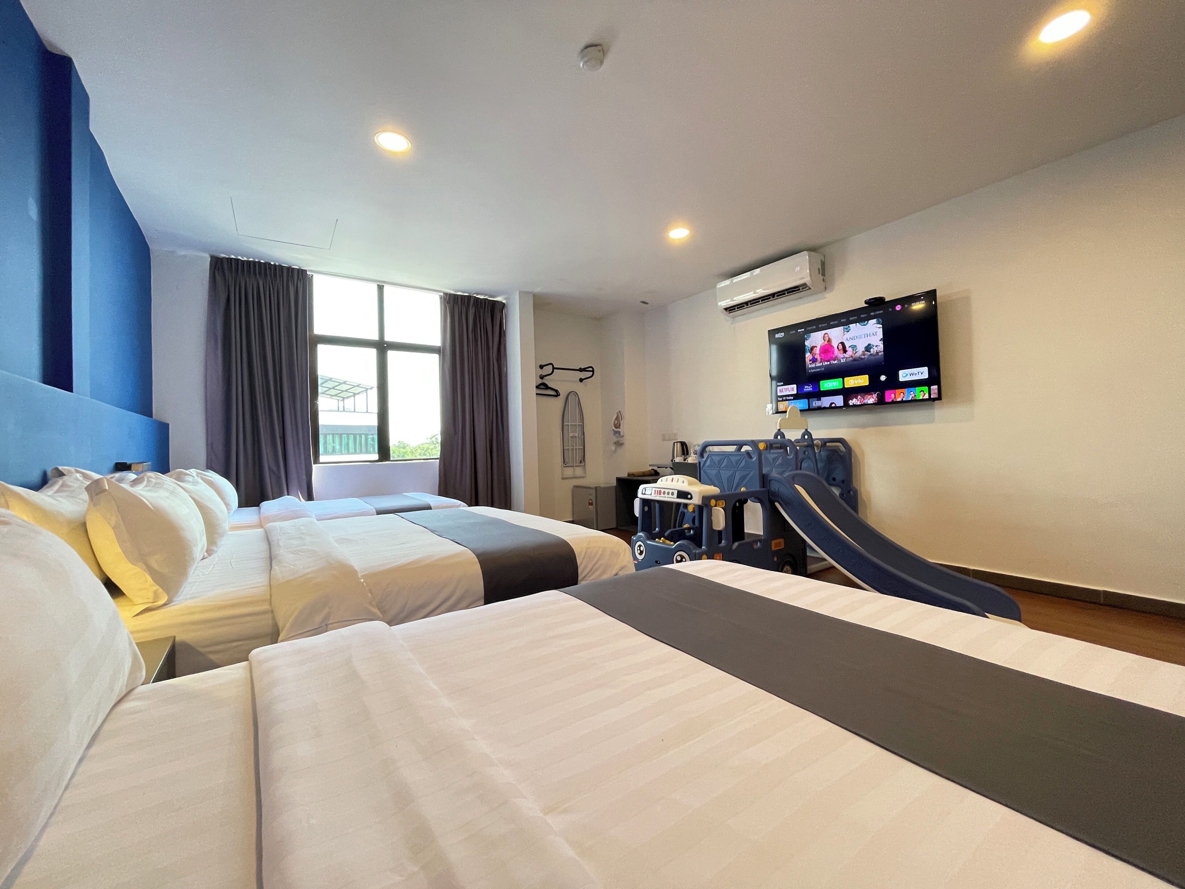 A hotel room with two beds, a TV, an air conditioner, and a children's play area.