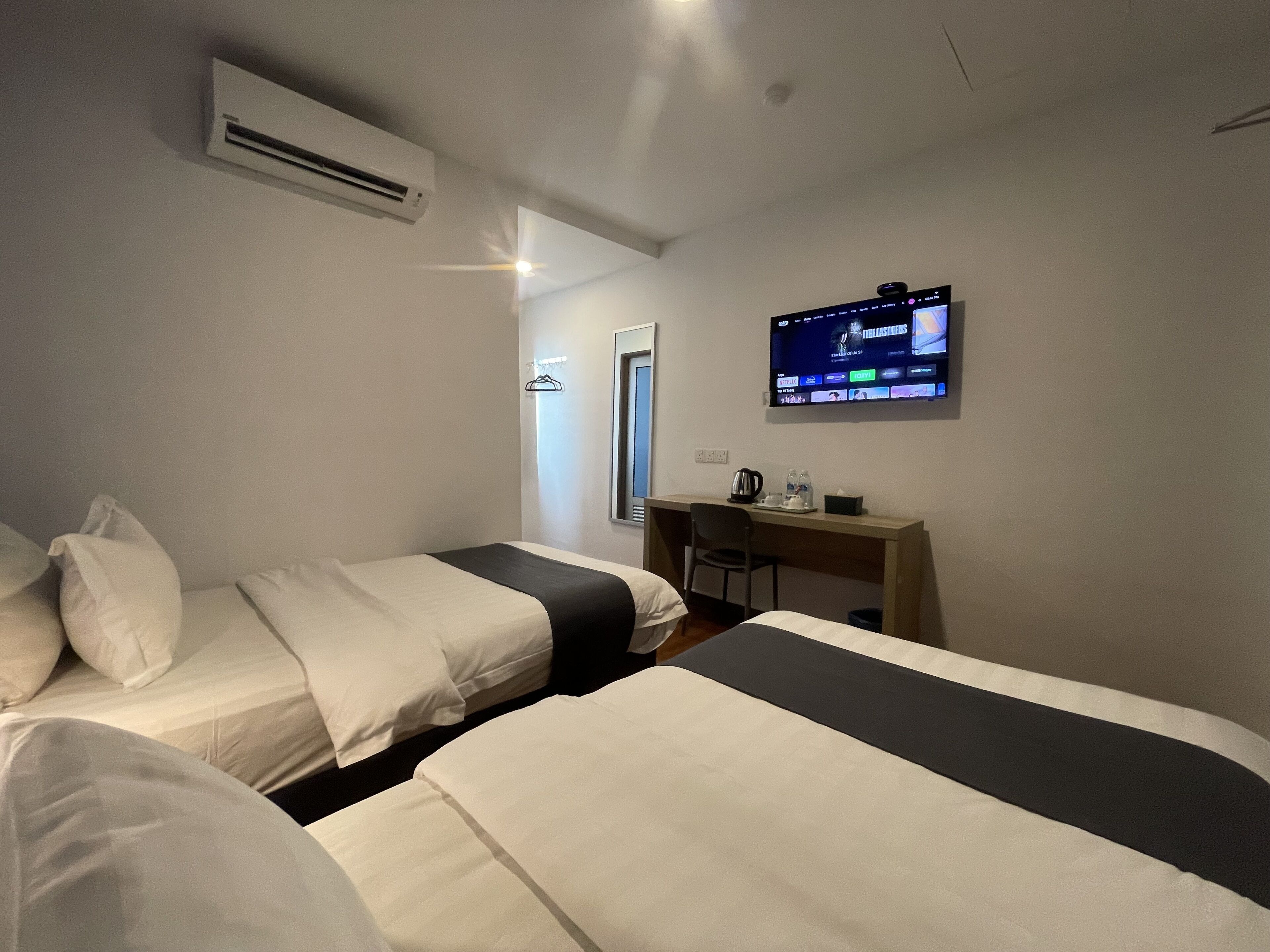 A hotel room with two beds, a desk, a chair, a TV mounted on the wall, and an air conditioning unit.
