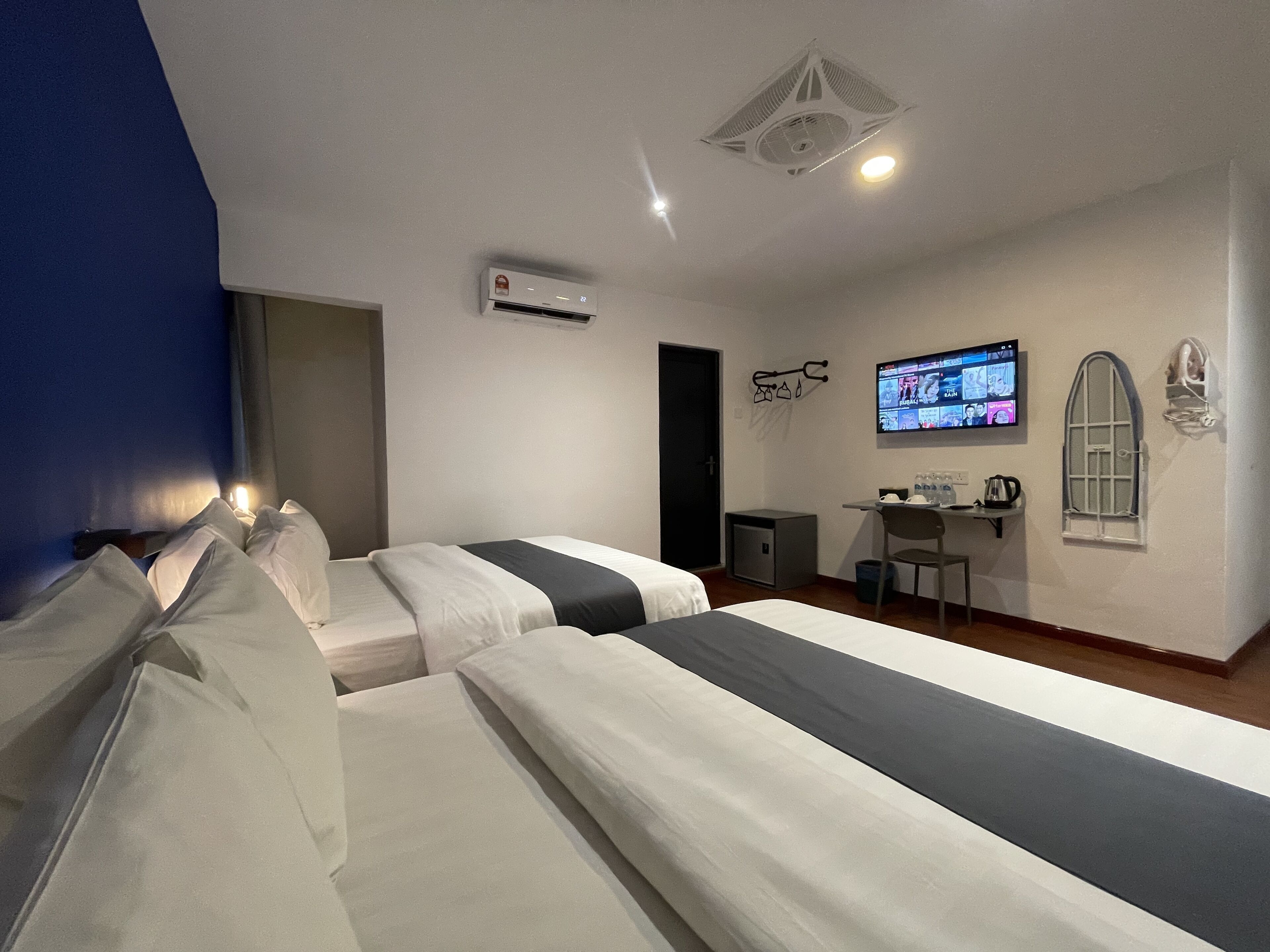 Habitación de hotel con dos camas, un escritorio con silla, televisor y una pequeña kitchenette.
