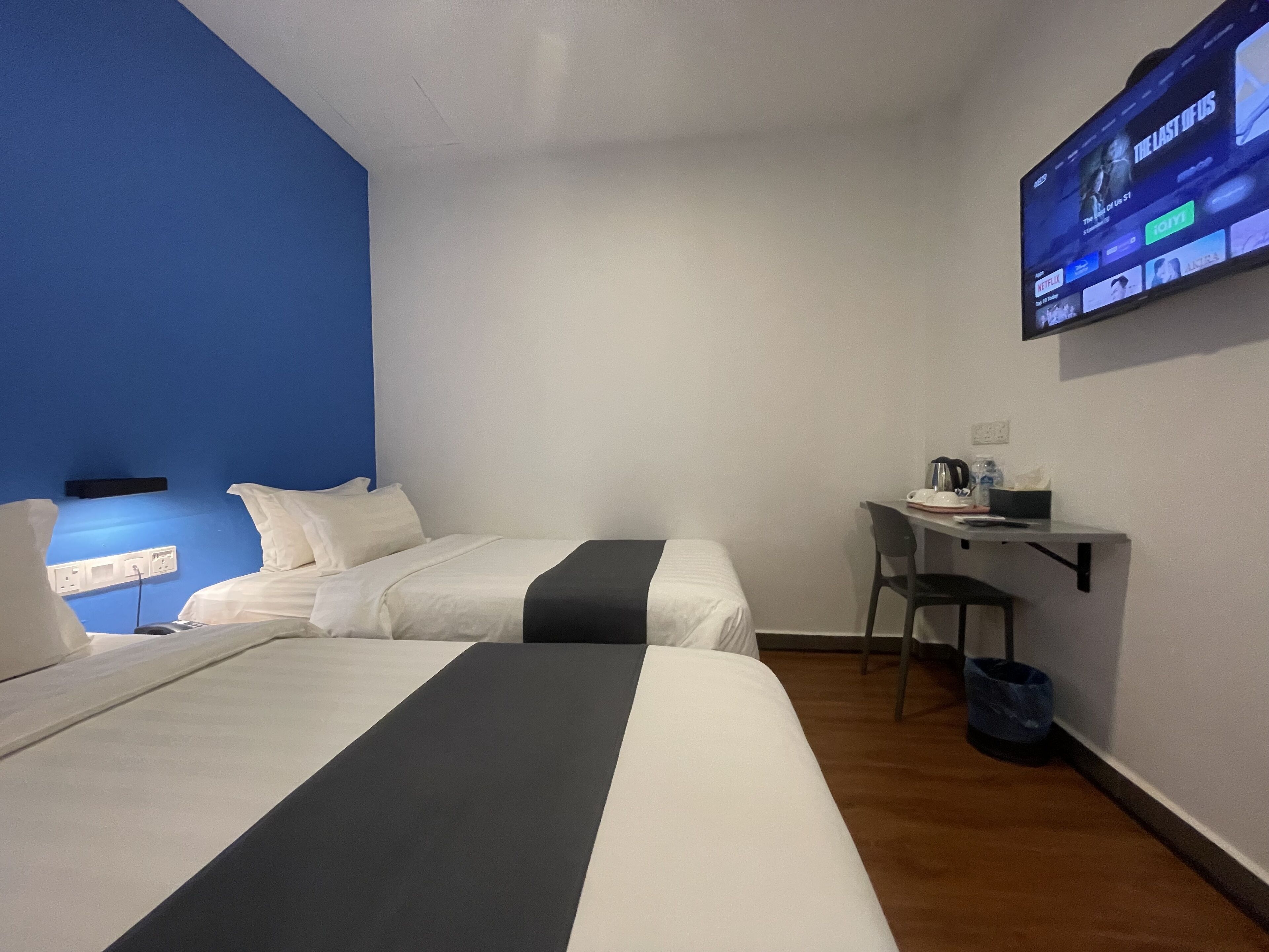 A hotel room with two beds, a desk, a chair, and a TV mounted on the wall.